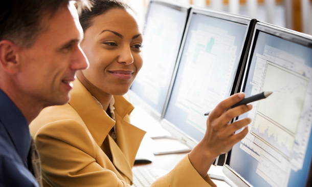 Photo showing two people looking at data on computer monitors.